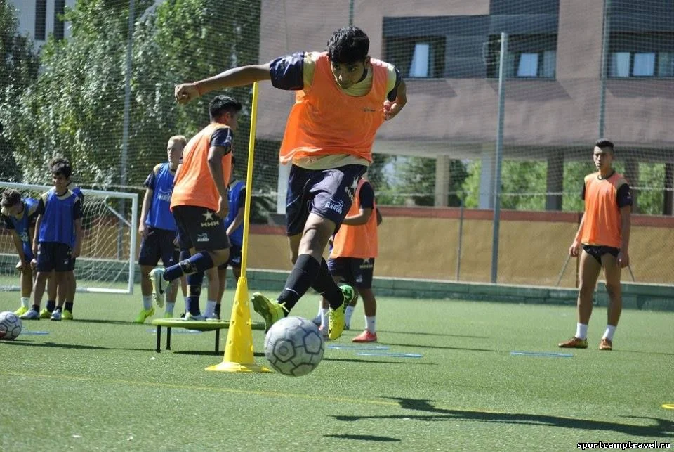 Jugador conduciendo el balón en un circuito técnico con petos naranjas